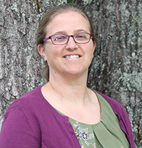 Professional woman wearing glasses sanding in front of a tree smiling