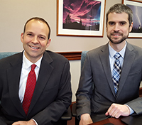 Two professional men wearing suits sitting next to each other in an office